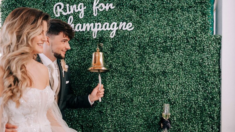 Bruidspaar-voor-muur-met-ring-for-champagne-Drink-The-Moment